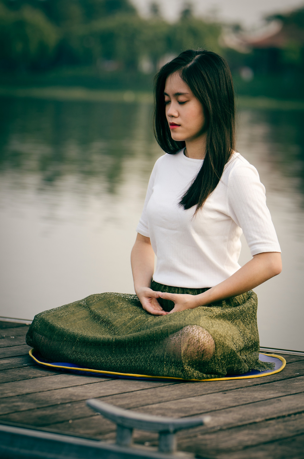 Chinese woman sitting a on dock outside focusing on her breathing techniques