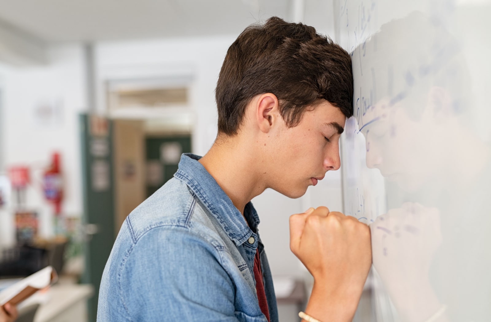 A stressed-out teenage boy pressing his head against a dry erase board at school