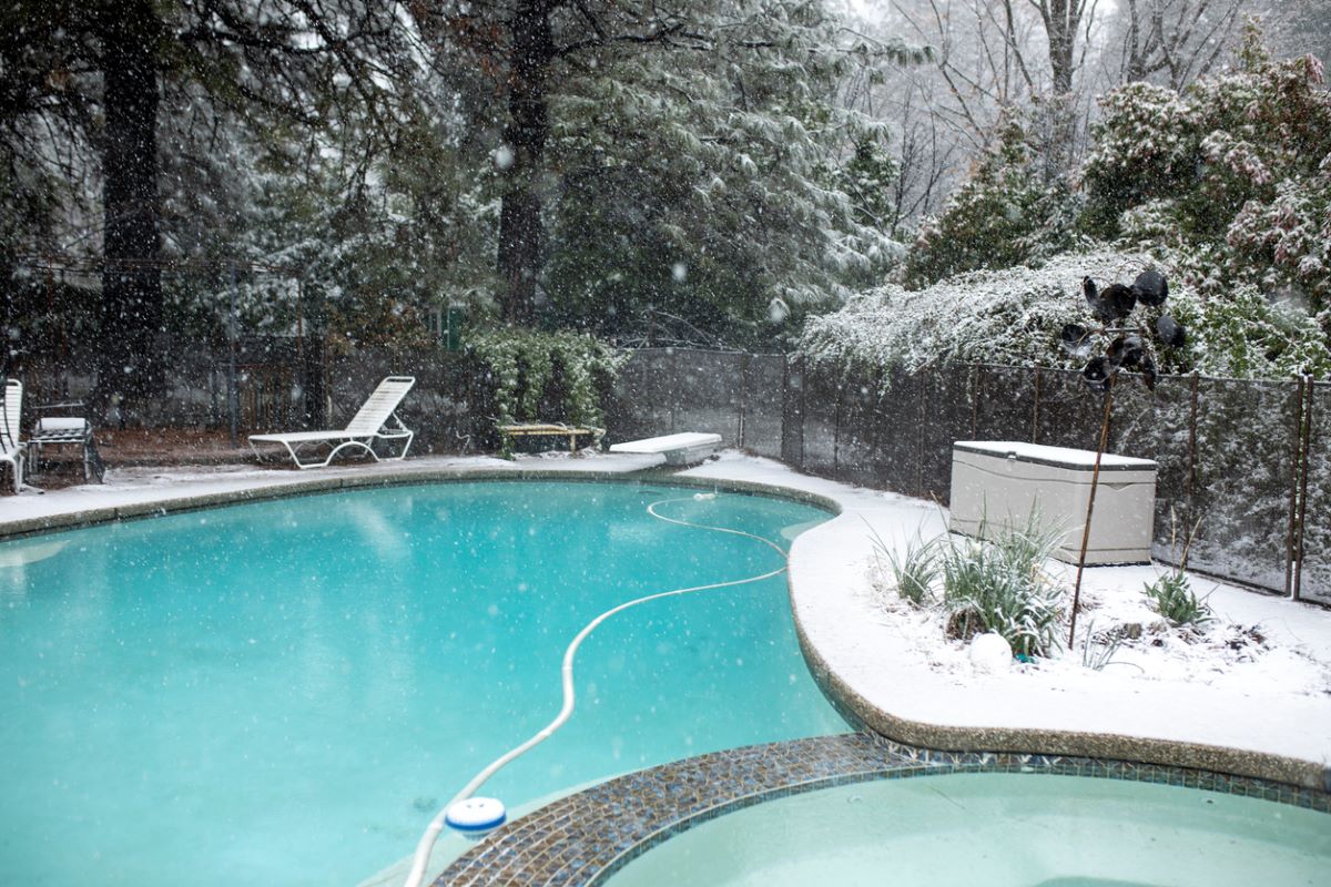 Backyard winter pool with clear blue water and snowy trees.