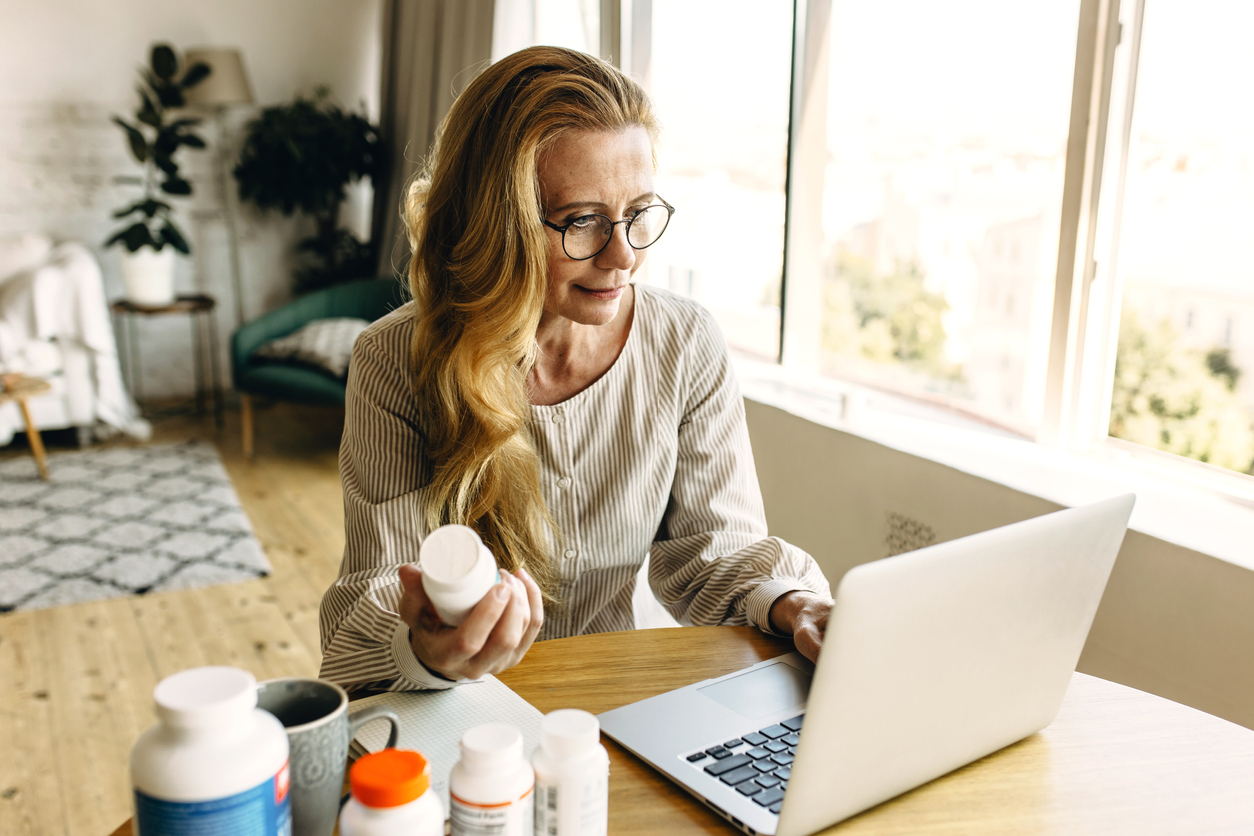 senior woman on laptop holding pills