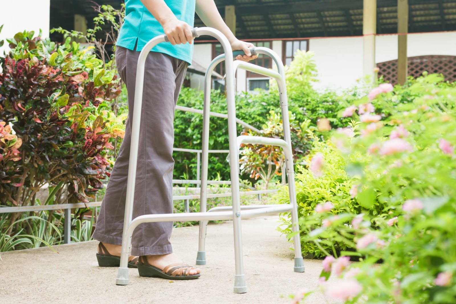 An elderly women uses a walker for walking while outdoors.