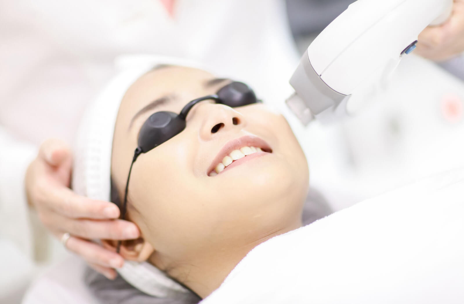 A young woman is wearing black eye caps and smiling as she undergoes an IPL procedure.