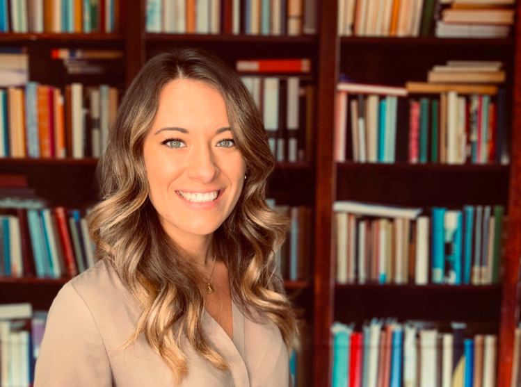 A professional headshot of lady with a wide smile with a library background