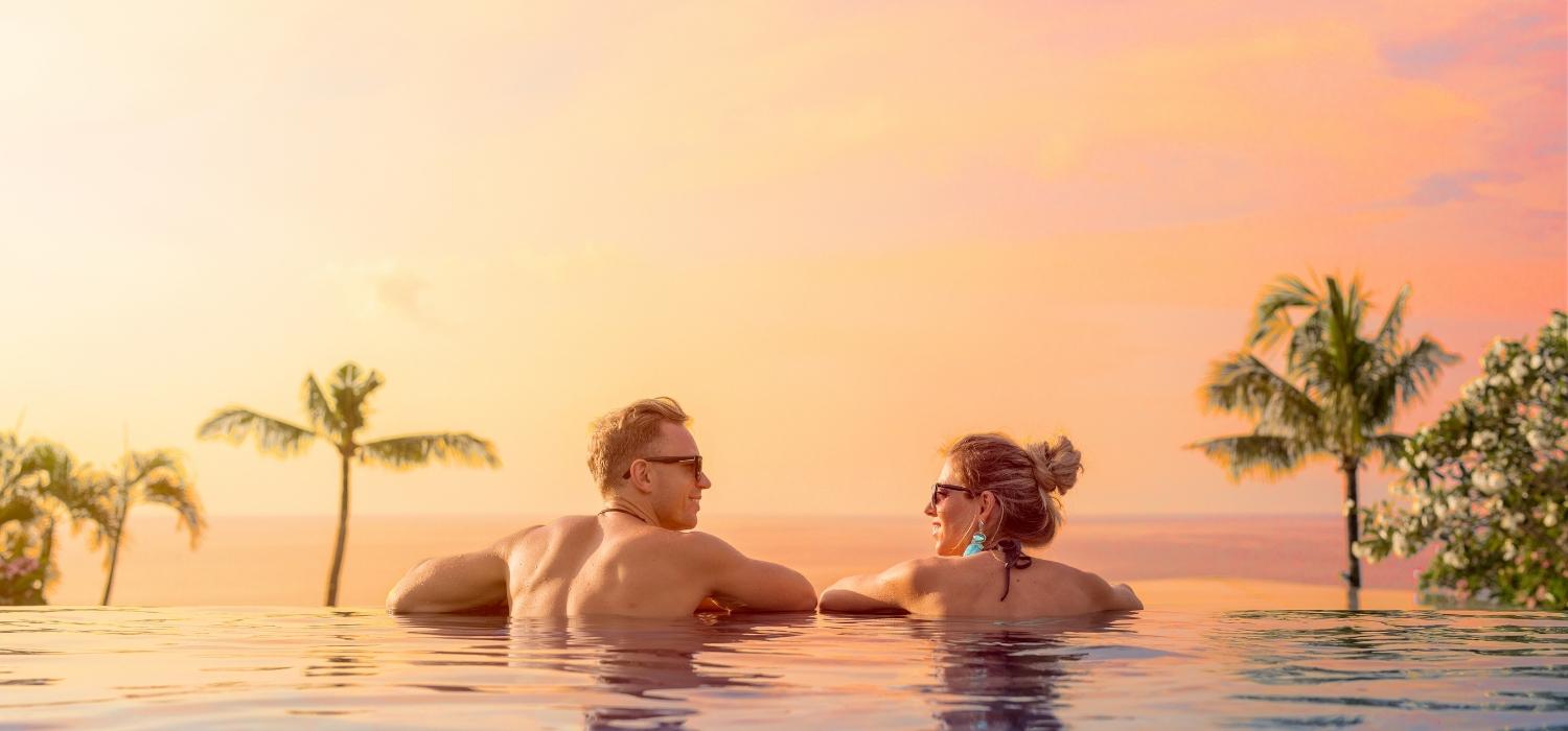 A couple swimming in the pool facing each other enjoying the sunset and wellness and sustainability in Bali.