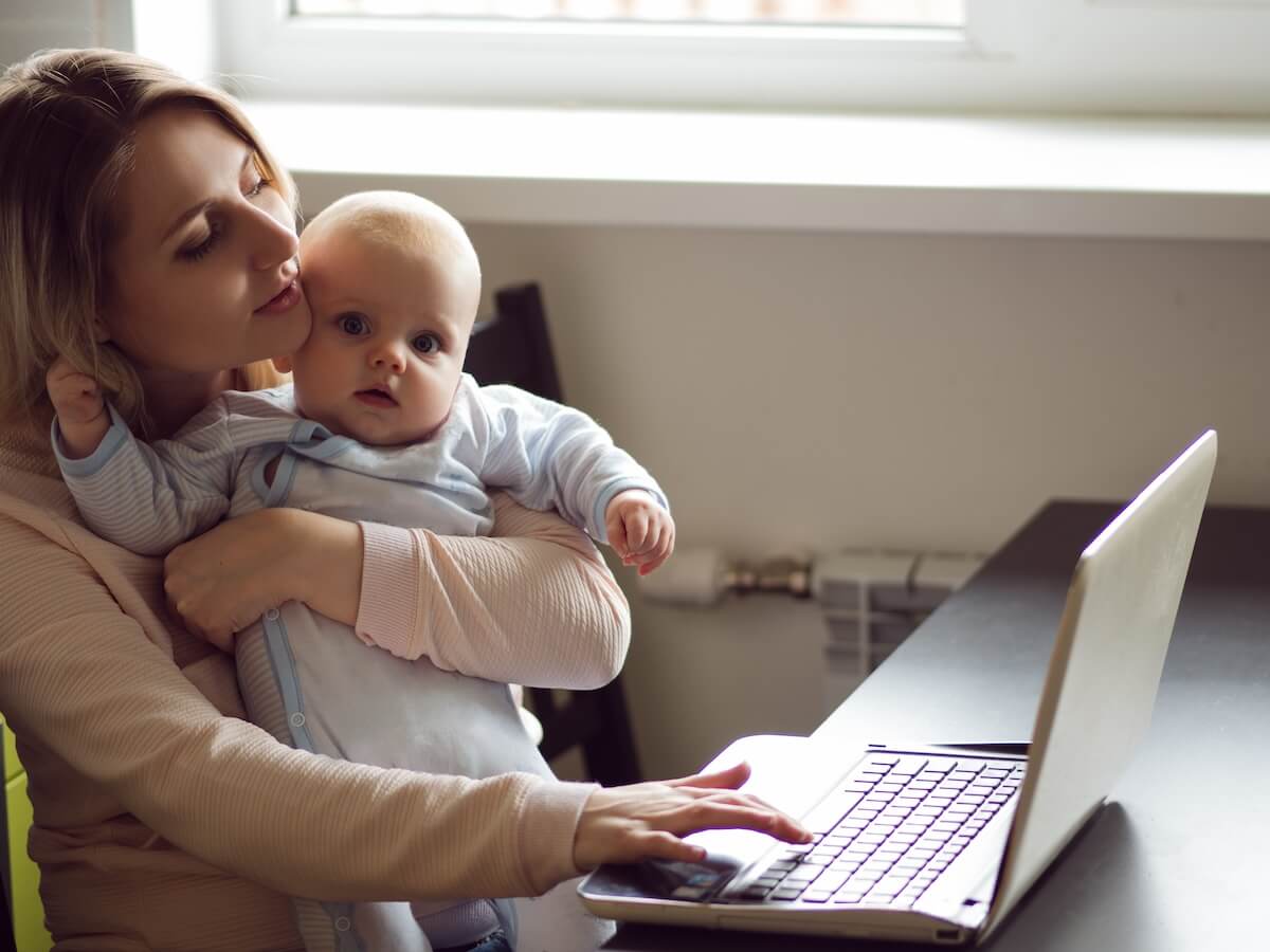Mother carrying her child while using a laptop