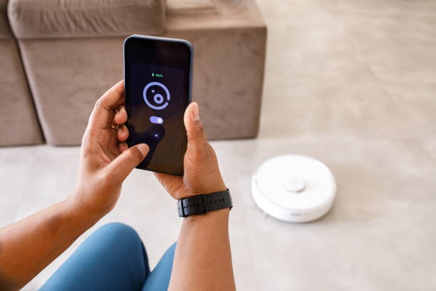 Young woman using smartphone to control smart vacuum cleaner robot Family interacting with smart home devices on daily activities smart vacuum cleaner stock pictures, royalty-free photos & images