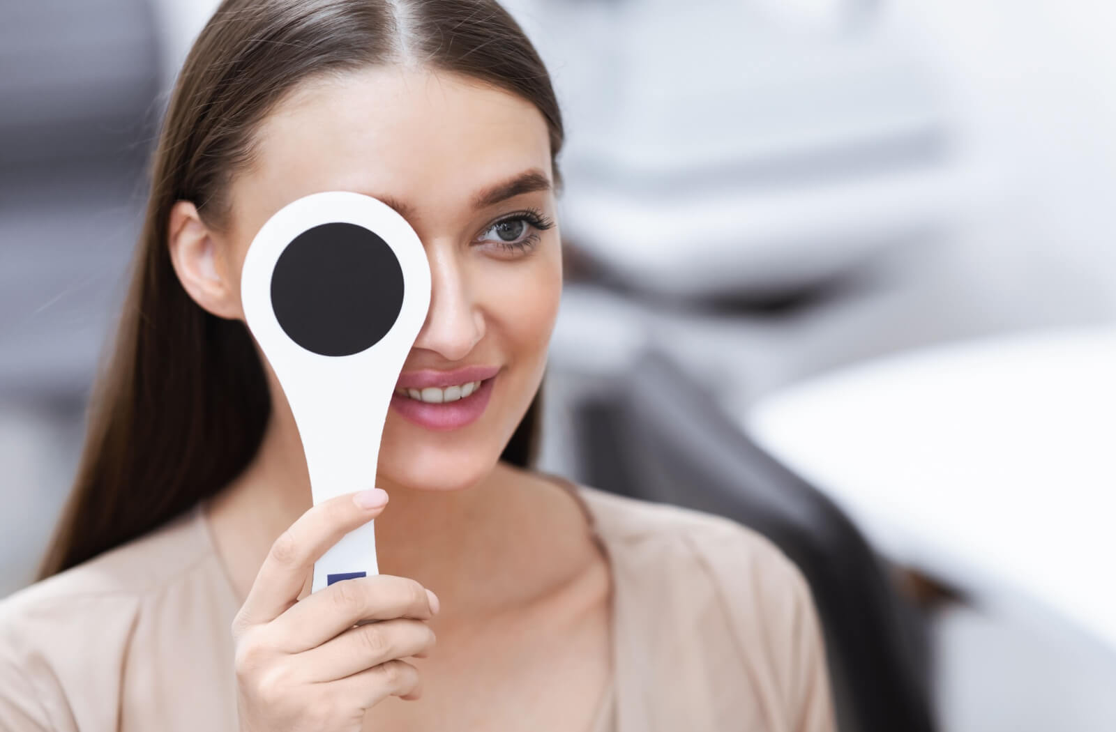 A woman holding an occluder against her right eye as a part of visual acuity test.
