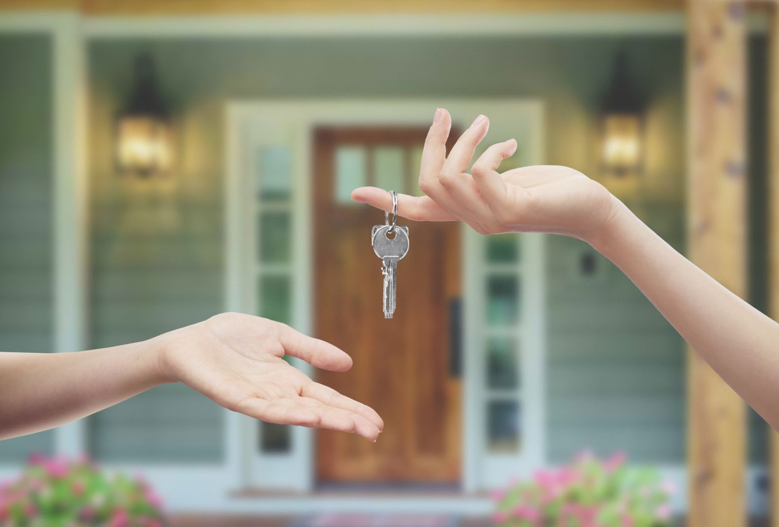 Two hands holding a key to a house, symbolizing ownership and access to a home.