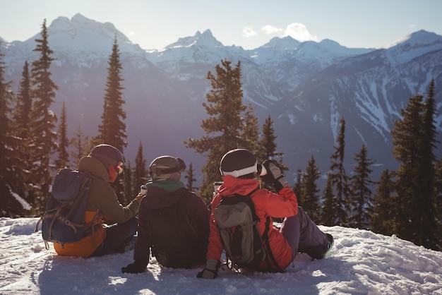 Free photo three skiers relaxing on snow covered mountain