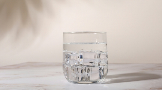 Glass of water with ice on a beige background