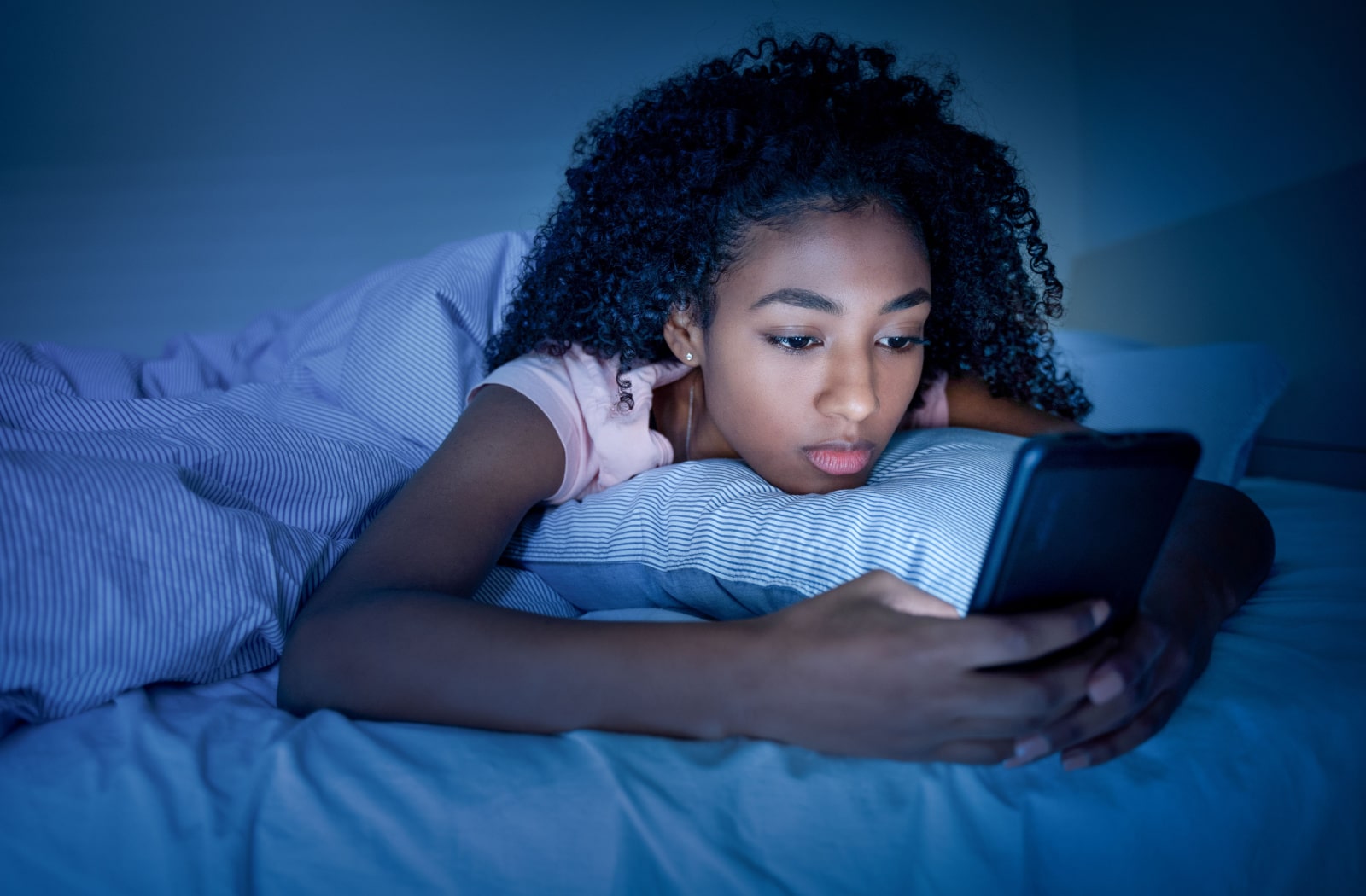 A teenage girl lies awake in bed playing on her phone because she can't sleep