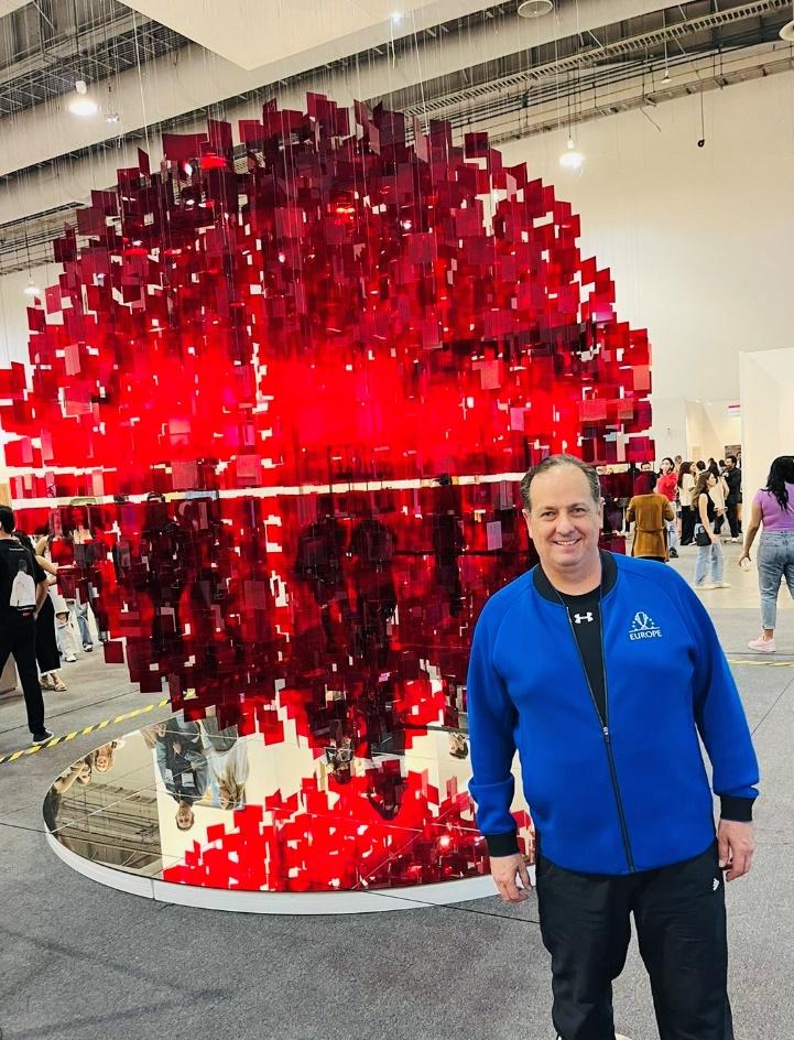 A person standing in front of a large red sculpture

Description automatically generated