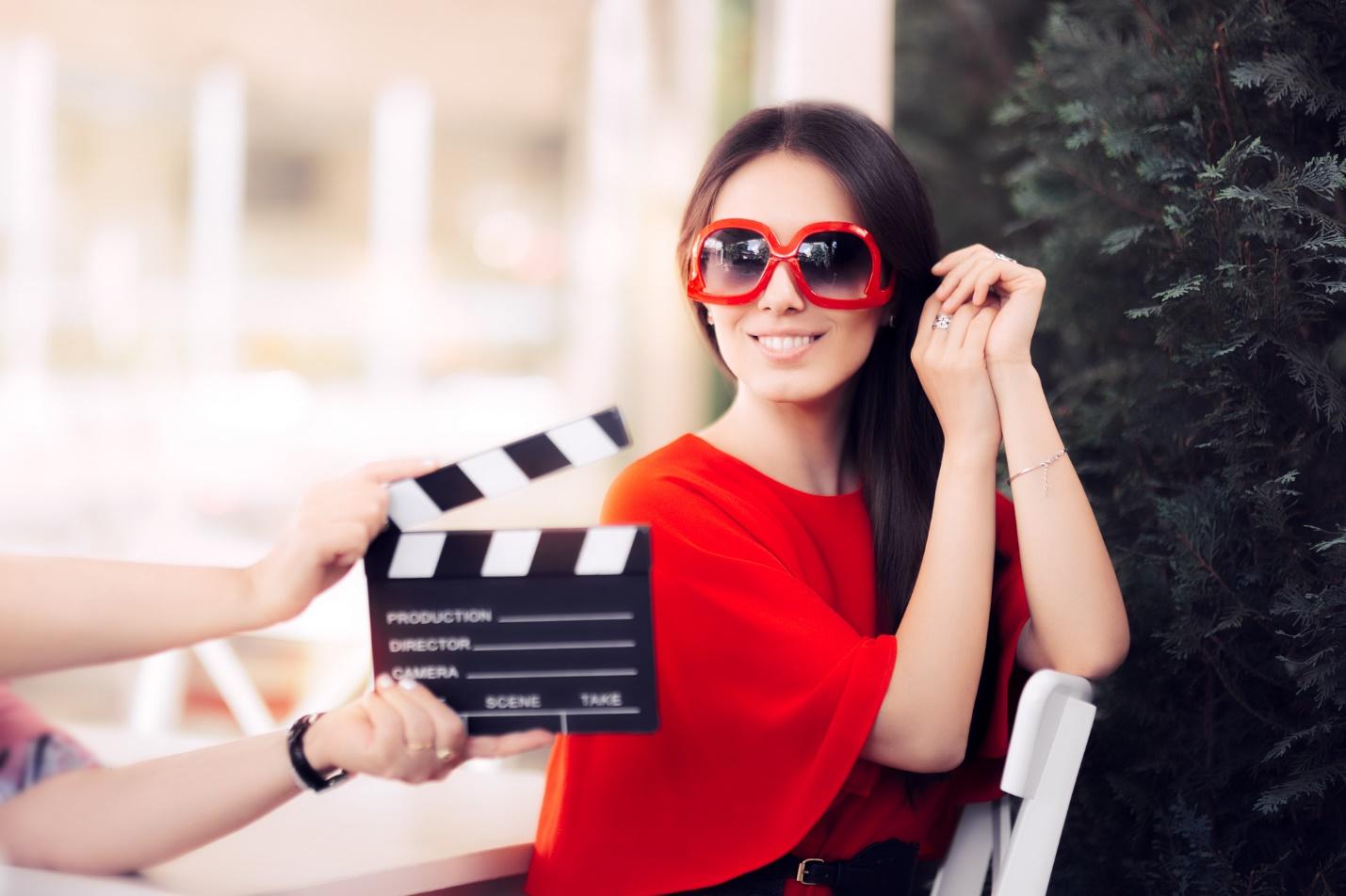 A person wearing sunglasses and holding a clapper board

Description automatically generated