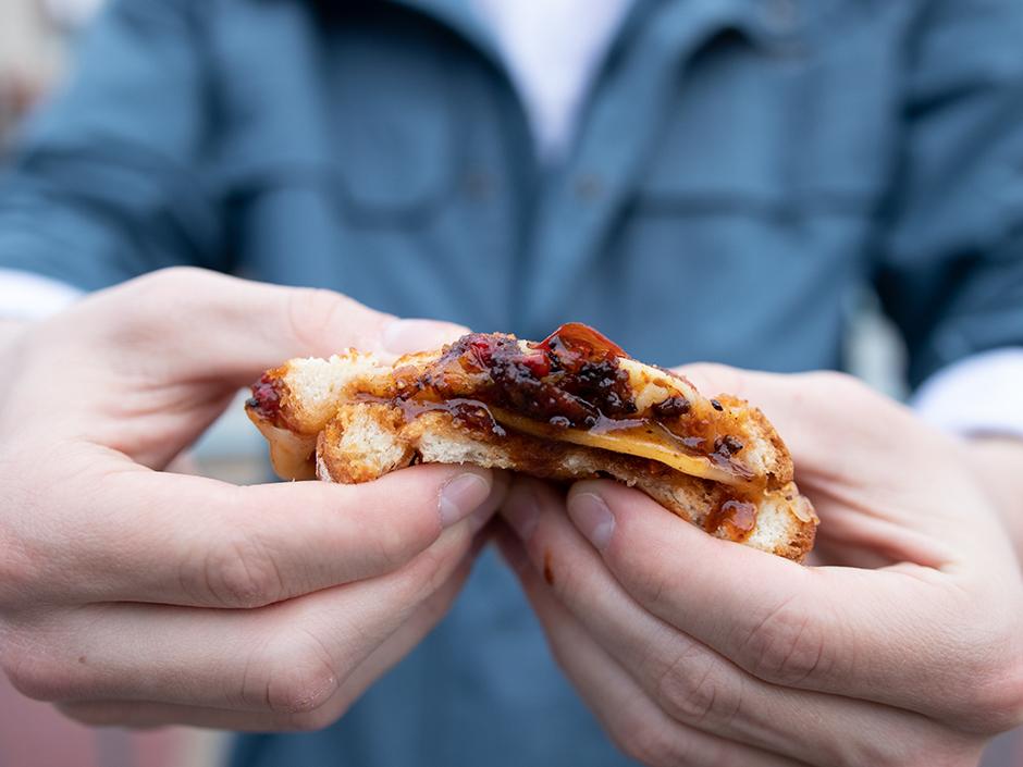 A person holding a piece the three cheese grilled cheese sandwich
