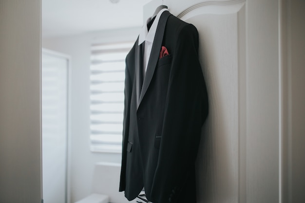 Черный костюм и белая рубашка свисают на вешалке от двери.