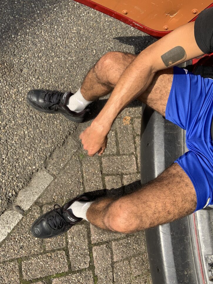 karim yoav sitting outside in blue shorts showing off his hairy legs