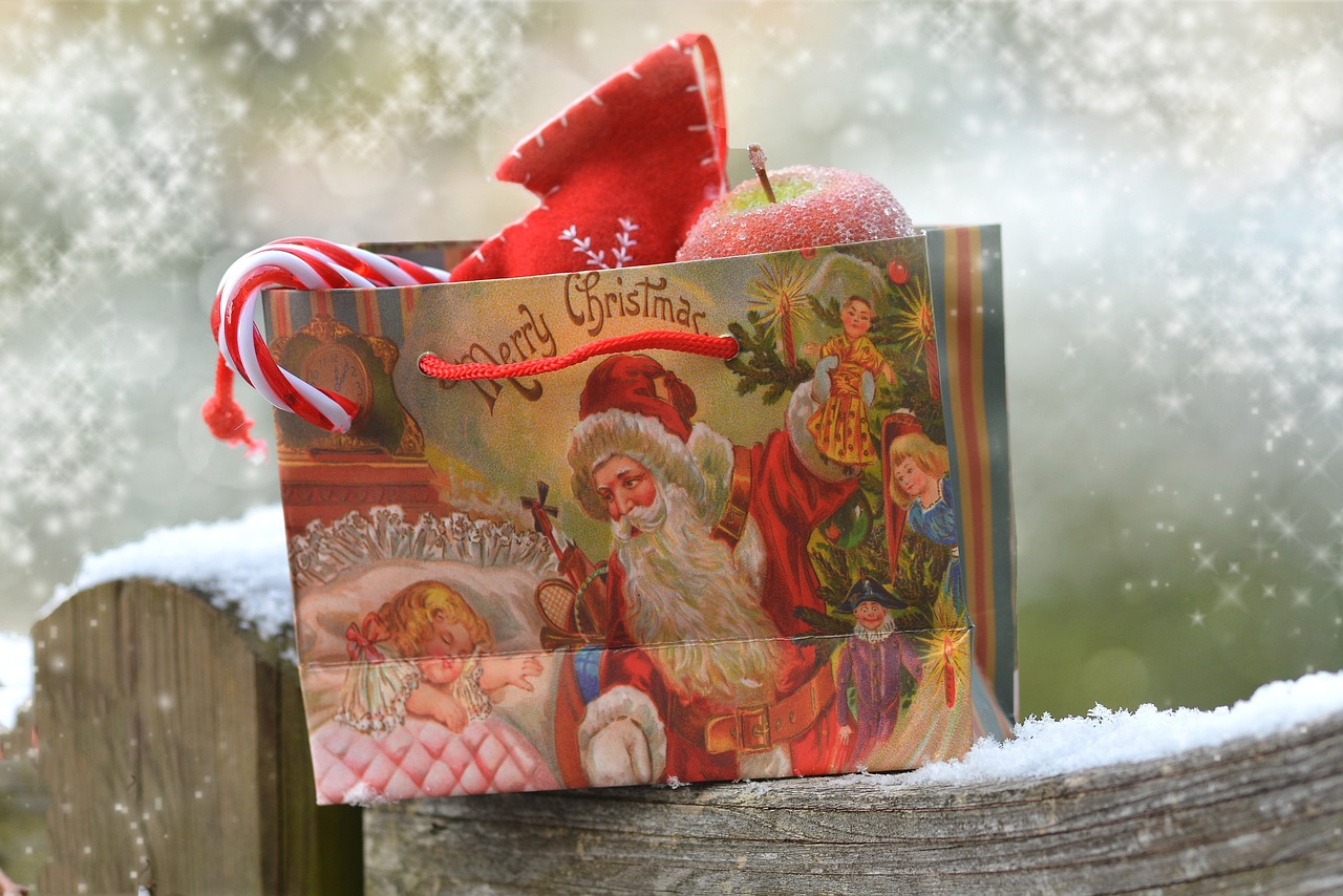 Alt Text: A Christmas gift bag on a fence post, with Santa and a little girl and a candy cane and an apple are sticking out of the bag.
