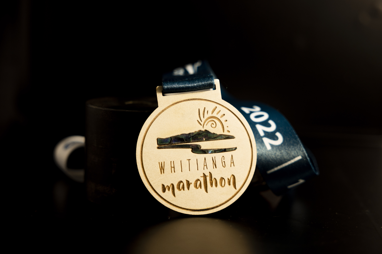 A custom wooden medal with paua shell, created for the 2022 Whitianga Marathon.