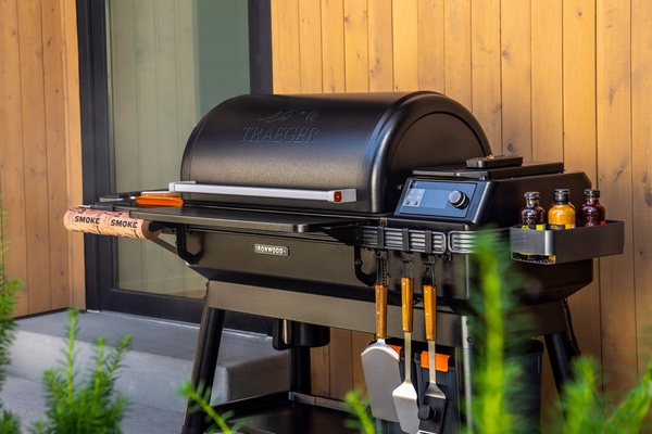 Traeger Ironwood XL with accessories attached on a cement patio with wood panel wall behind the grill.