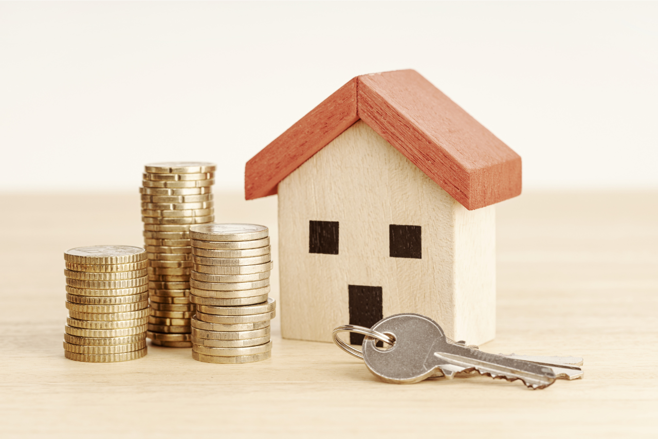 A small toy house placed adjacent to a stack of coins and a key, symbolizing homeownership savings.