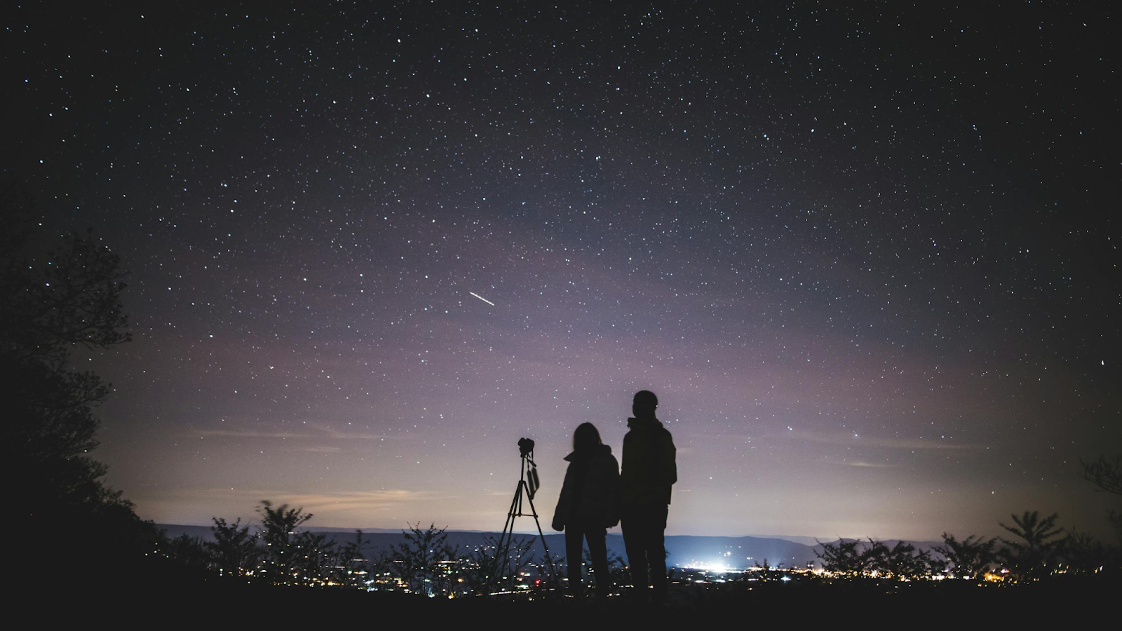 Two people stargaze outside of a city