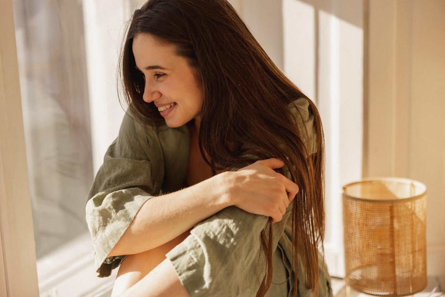 C:\Users\DELL\Downloads\happy-young-caucasian-girl-with-smile-face-looks-out-window-while-sitting-windowsill-morning-brunette-with-long-hair-wears-green-loose-shirt-concept-rest-recovery.jpg
