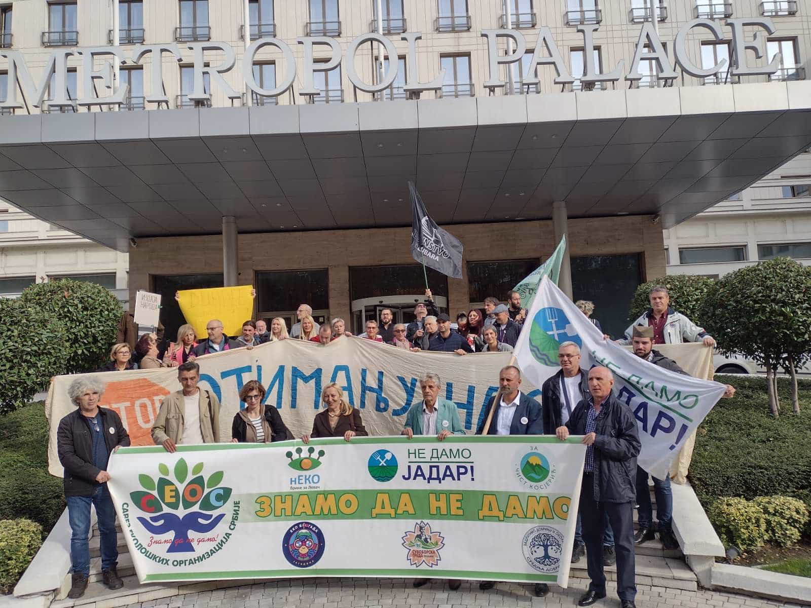 Protesters from various groups hold banners outside a posh hotel.