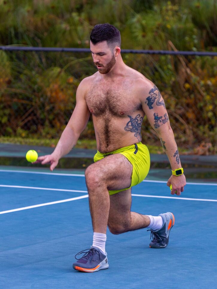 Dillon Cassidy on the tennis court shirtless wearing running shoes and yellow sweat shorts