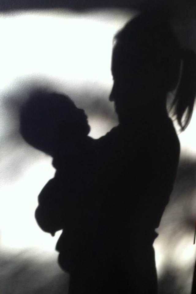 A silhouette of a person holding a baby

Description automatically generated