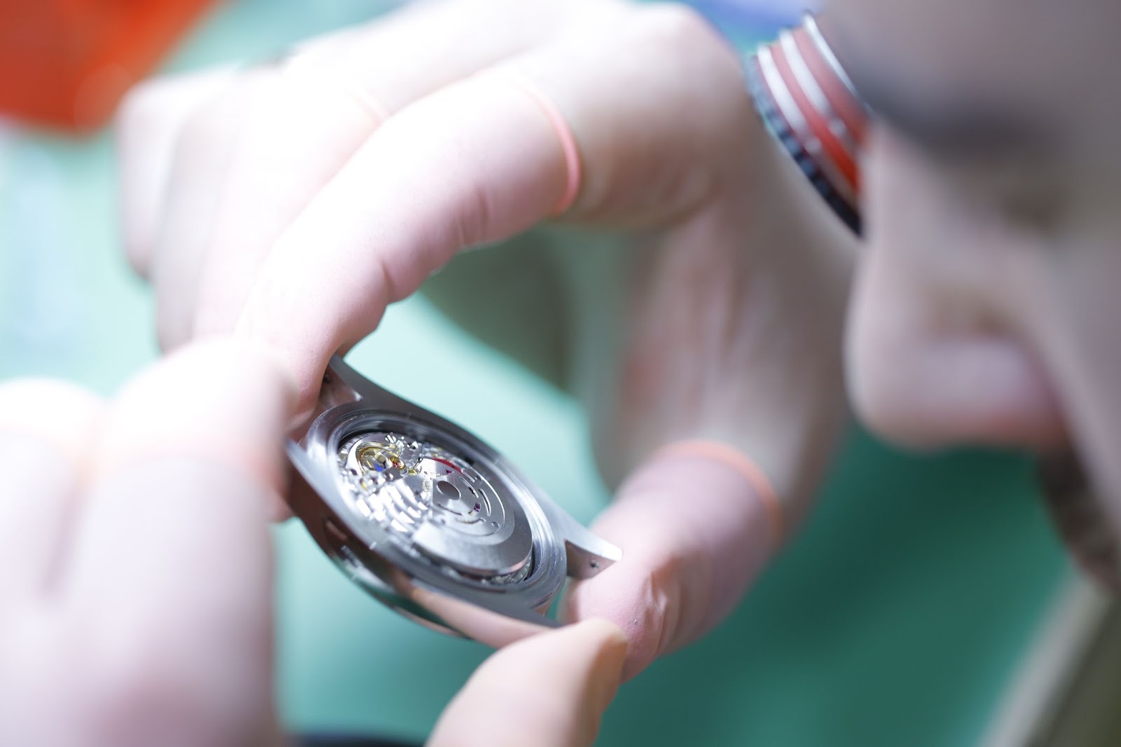 An image showing a watch's inner movement prior to being serviced within Chronostore's in-house repair department, examined by a professional watchmaker wearing finger tip gloves for the watch's protection, all above a pale green desktop.