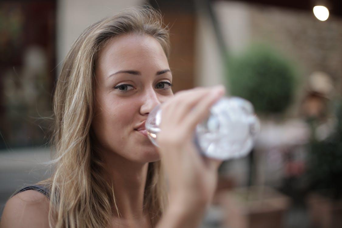 Free Selective Focus Photo of Smiling Woman Drinking Water from a Plastic Bottle Stock Photo