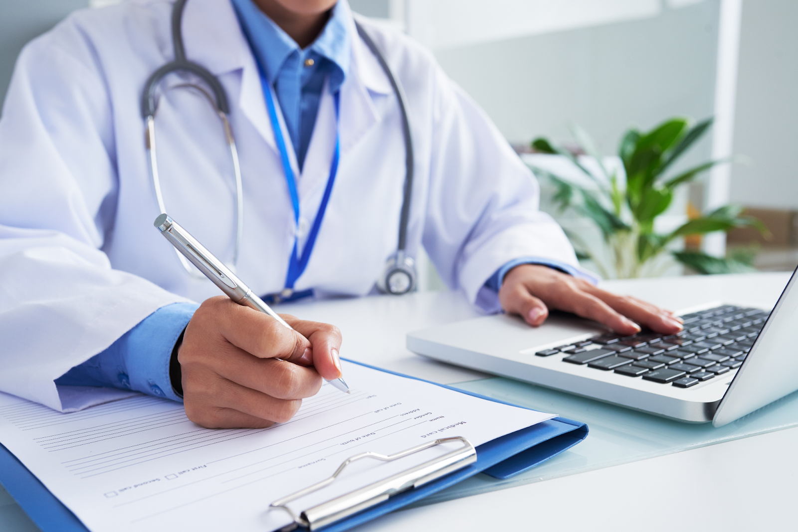 mãos de um médico escrevendo no formulário e digitando no teclado do notebook