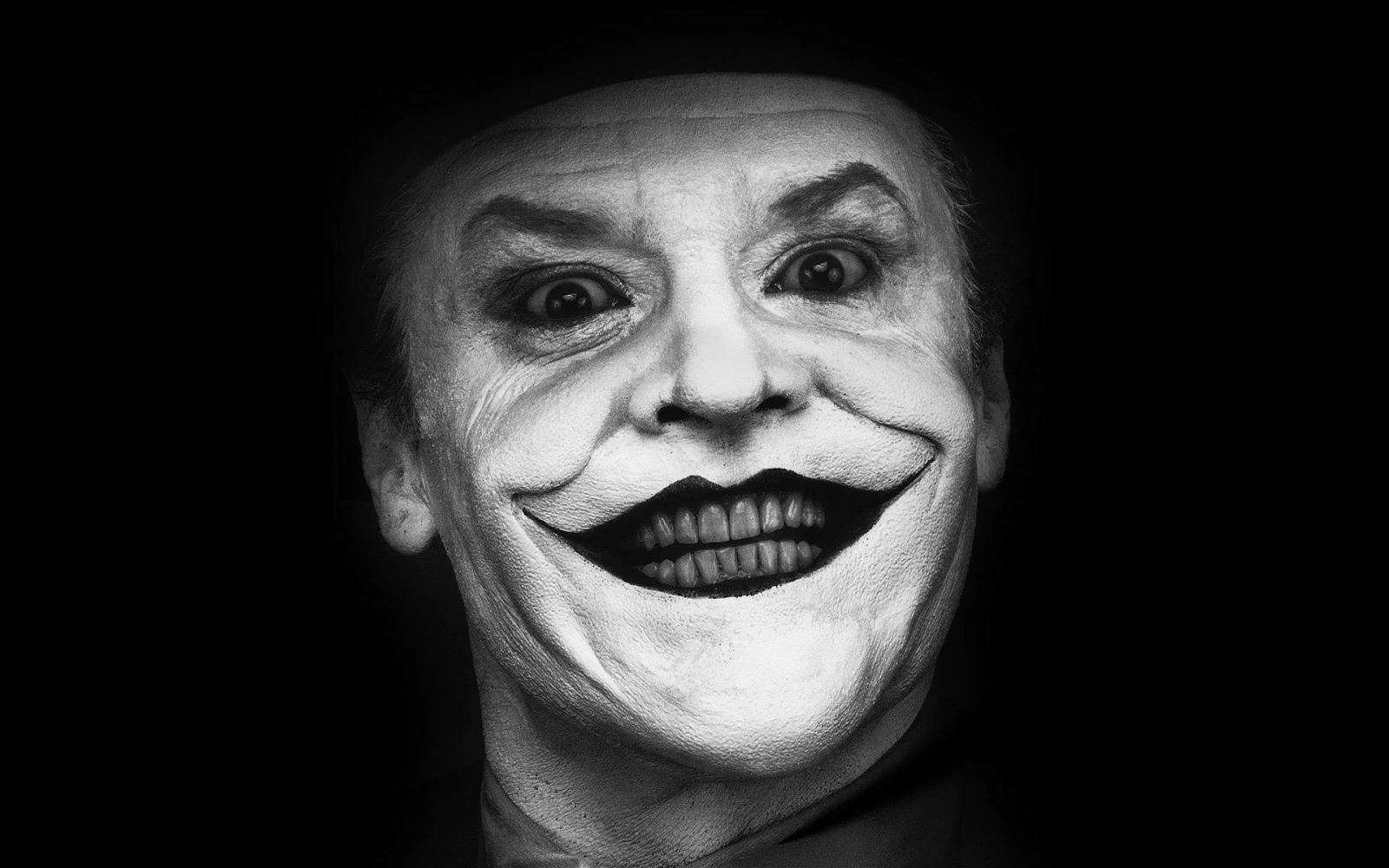Jack Nicholson como el Joker, sonriendo de manera macabra en una imagen en blanco y negro. Se ve su rostro de cerca y el fondo negro