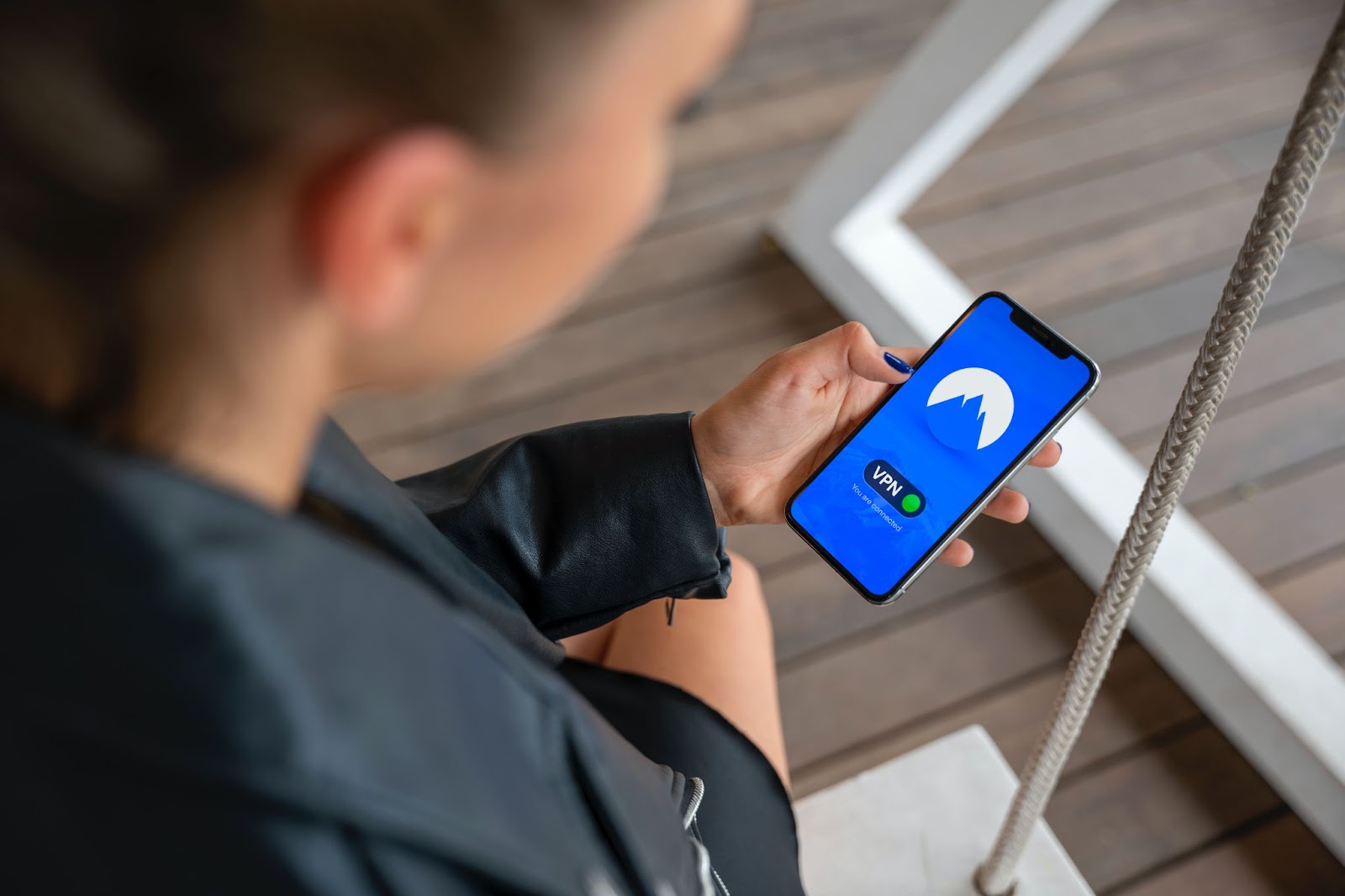 Alt-text: A woman confidently holds a smartphone in her left hand, featuring a security app with a sleek blue interface. The app prominently showcases the word "VPN" in crisp white lettering.