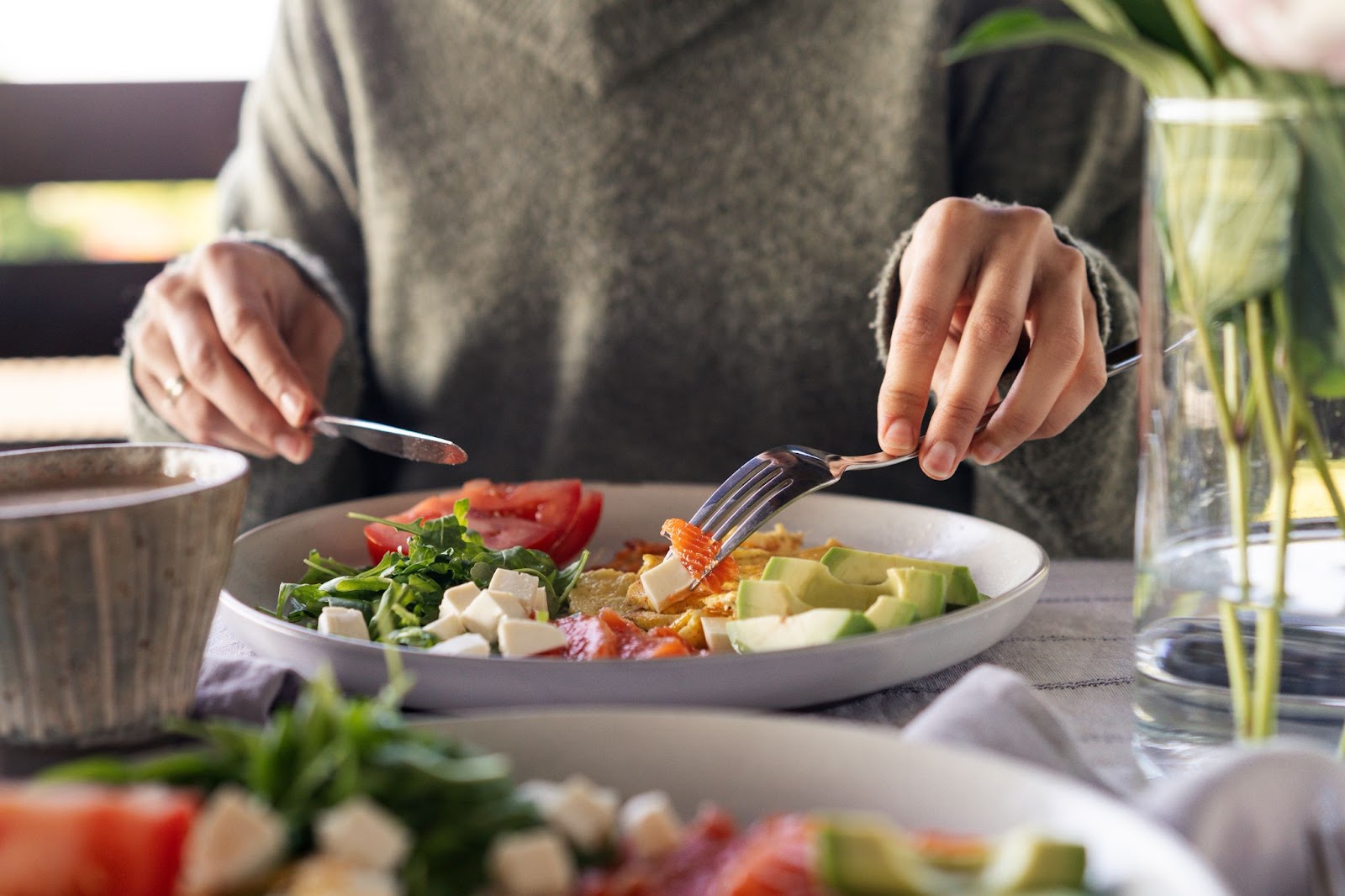 women eating a healthy meal of salmon, avocado, tomatoes, leafy greens and omelette