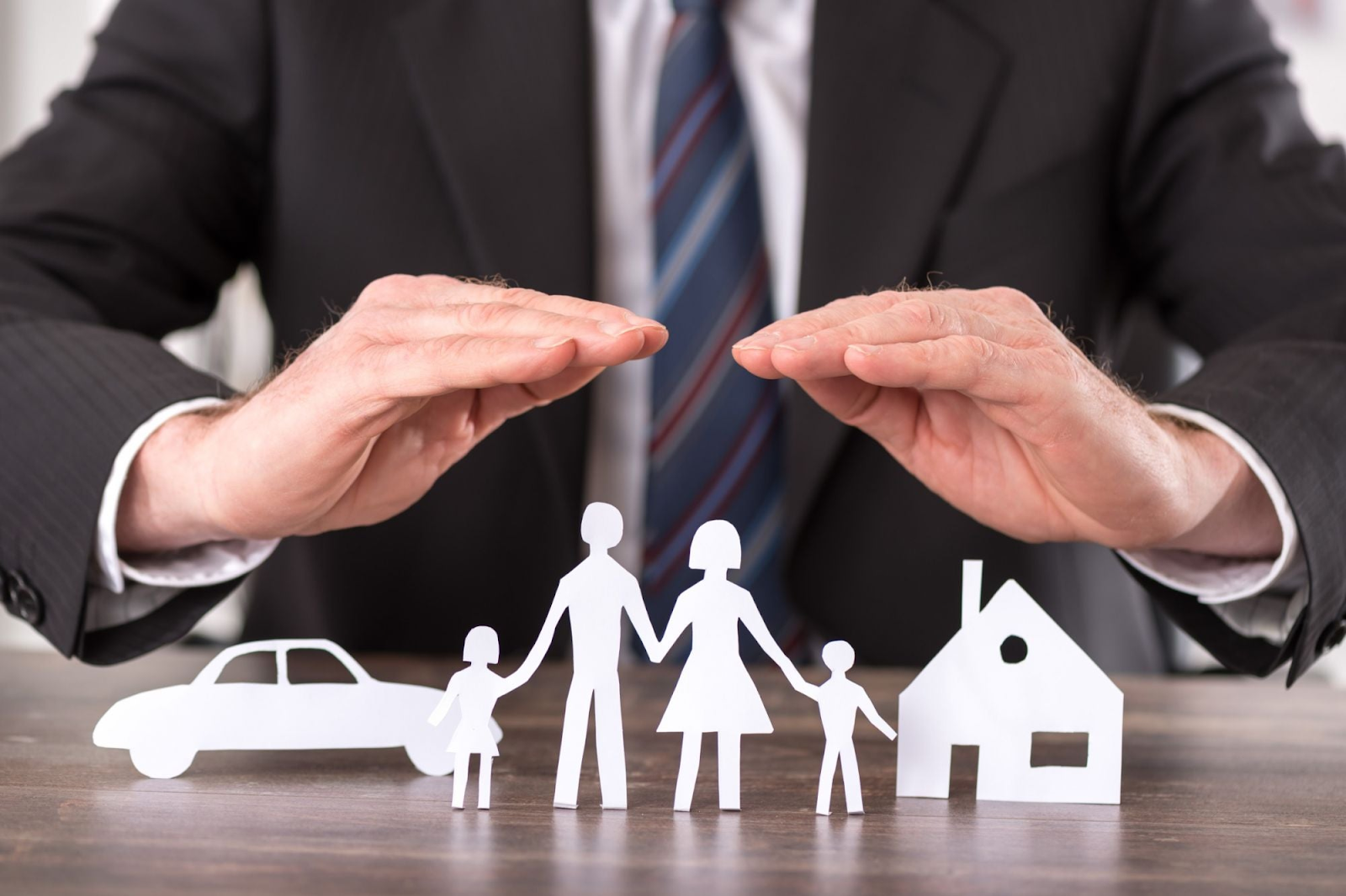 Insurance agent with hands ouver a cutout of a family, a car and a house. Life insurance