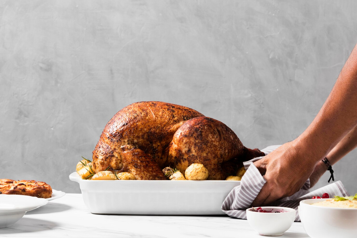 A person placing roasted Turkey on the Friendsgiving table.