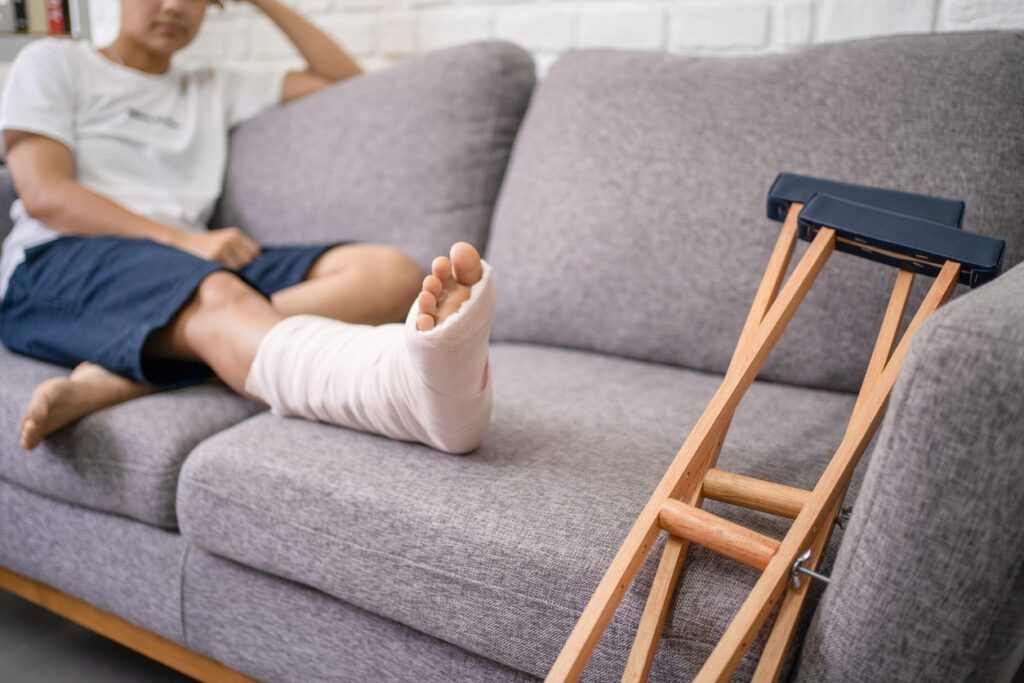 Woman resting broken foot on couch next to crutches. Our Houston personal injury lawyers defend those injured by others negligence. 