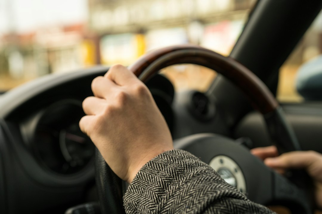 A person with two hands on the steering wheel of a car 