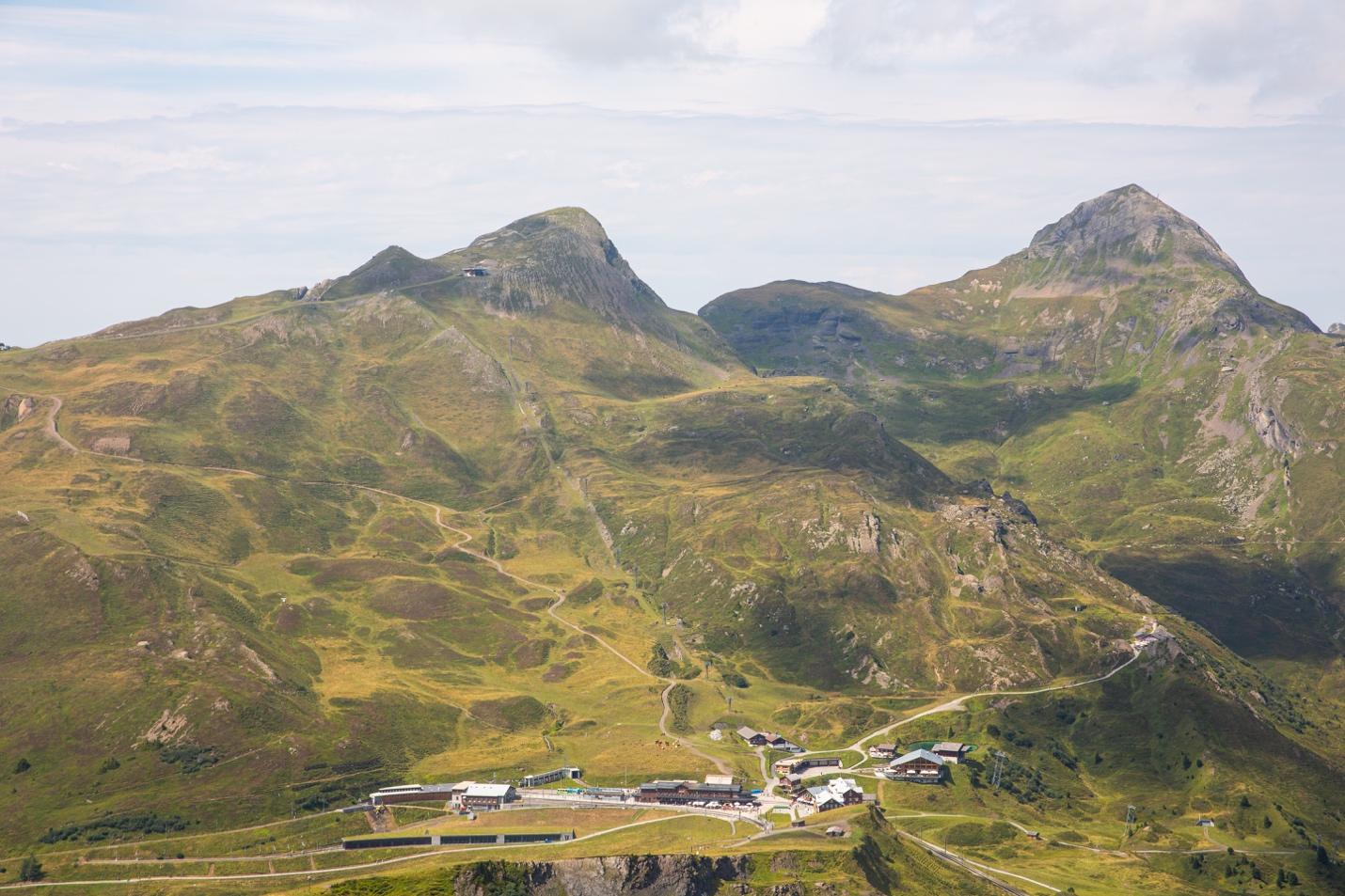 A green mountain range with buildings and a road

Description automatically generated