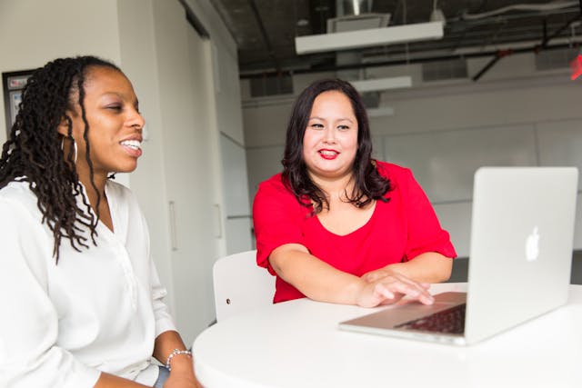 Two women sitting at a table looking at a laptop