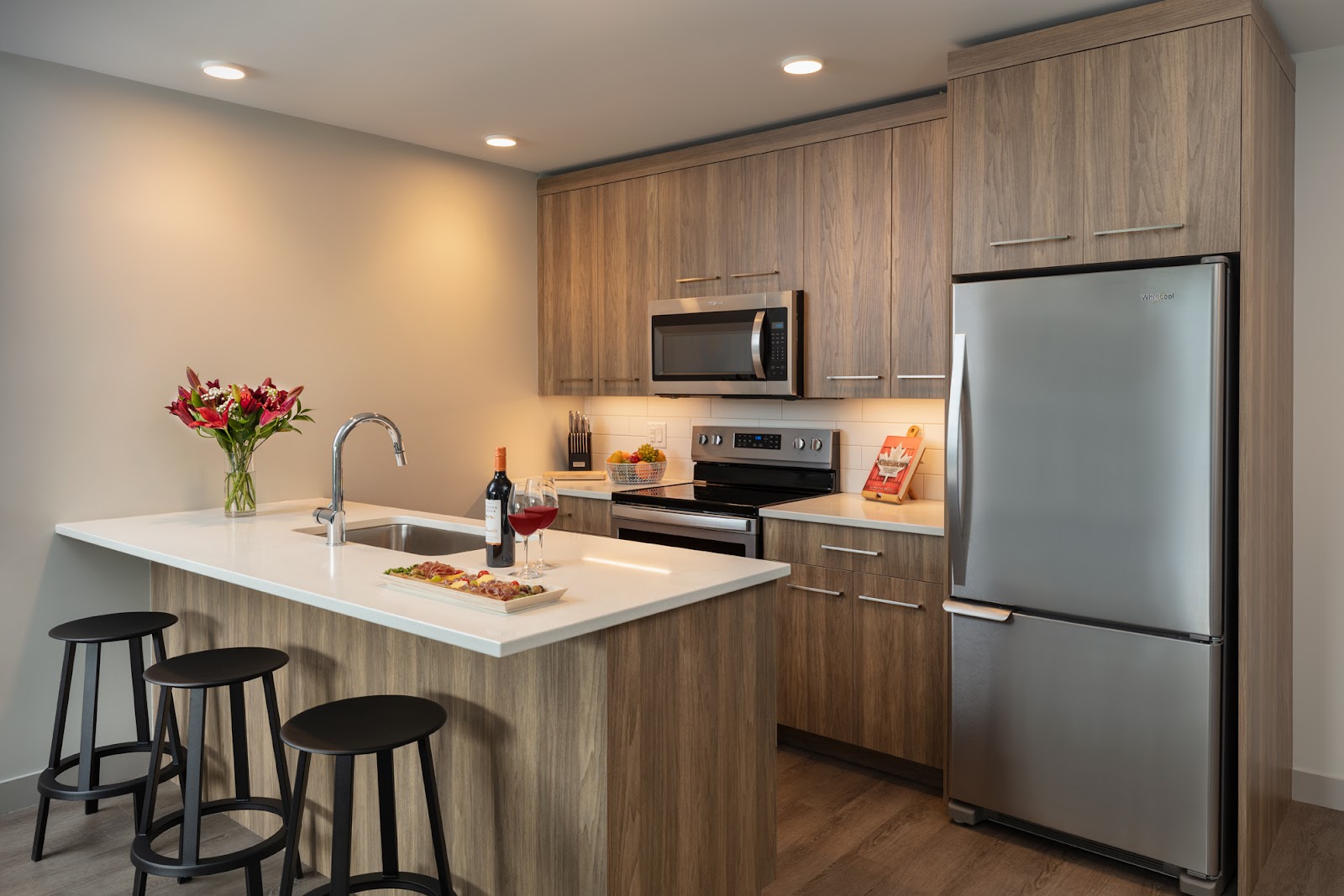 a full in-suite kitchen at The Shore Kelowna apartment hotel, with wooden cabinets, a large kitchen island, and stainless-steel appliances