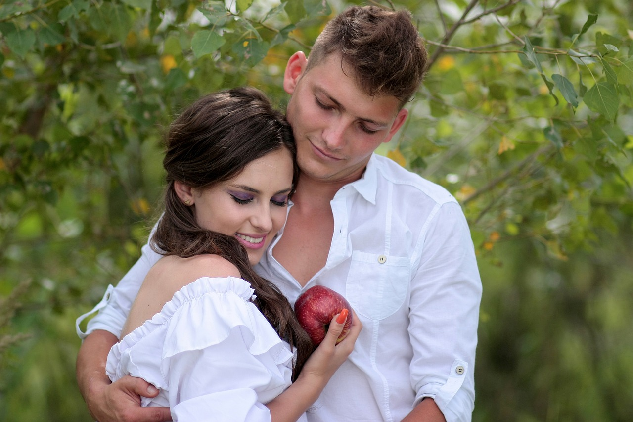 A man and woman in white holding an apple and hugging