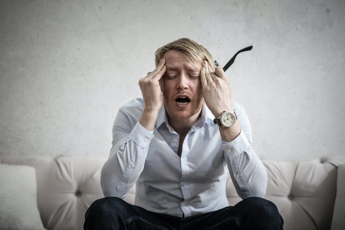 a man holding his head and glasses in severe headache pain