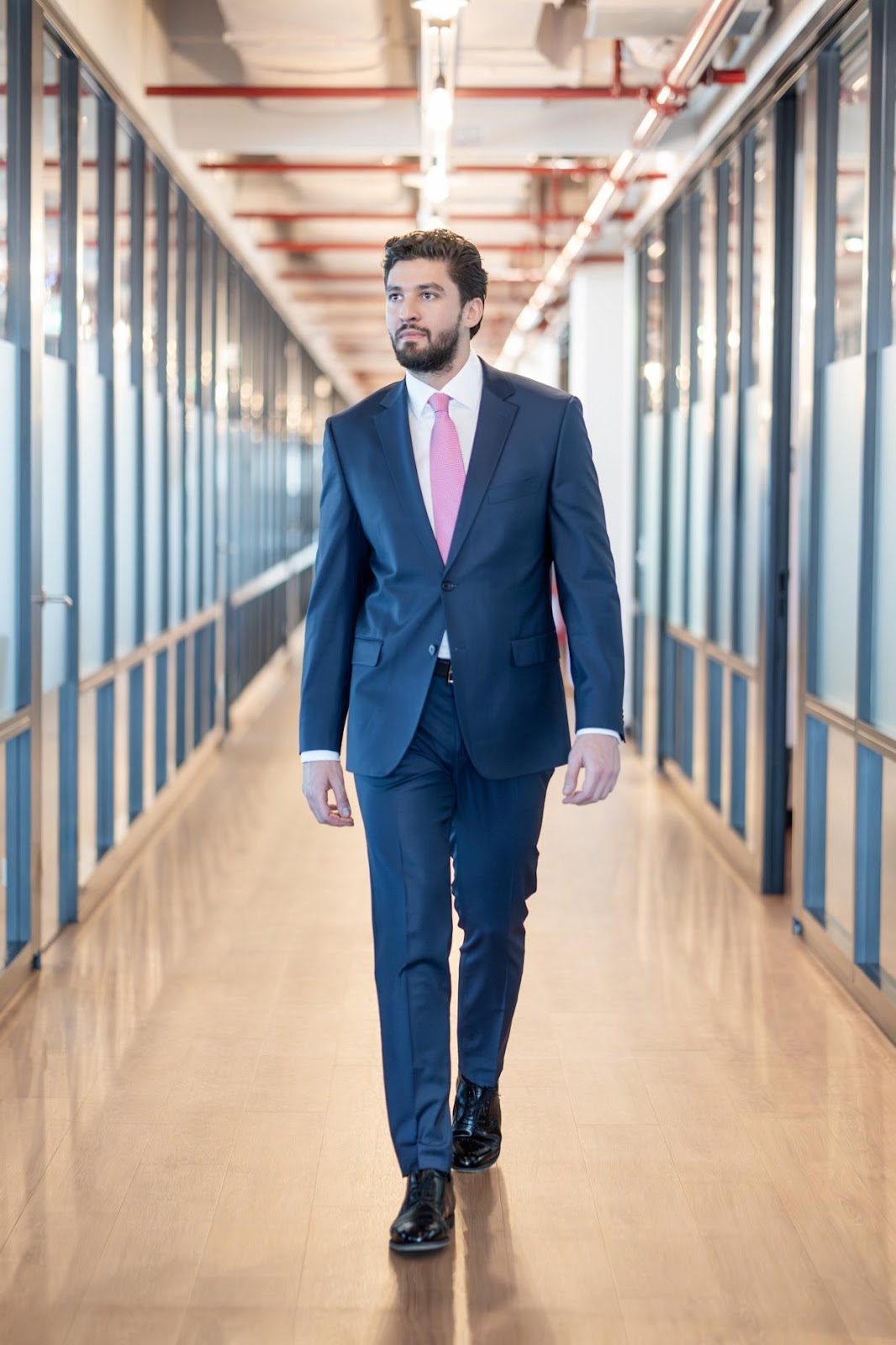 A person in a suit walking down a hallway

Description automatically generated