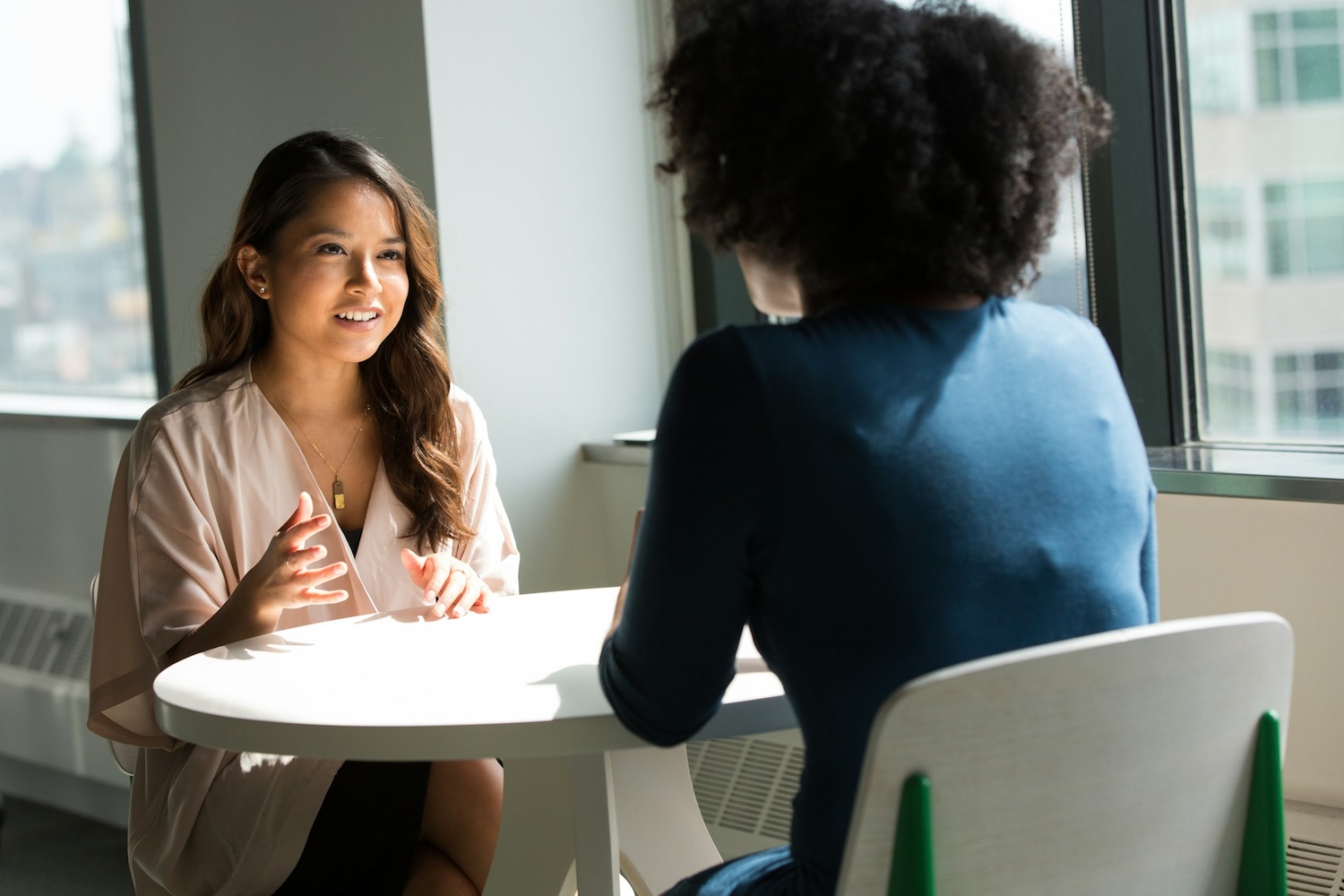 women of color talking at small white table in office setting