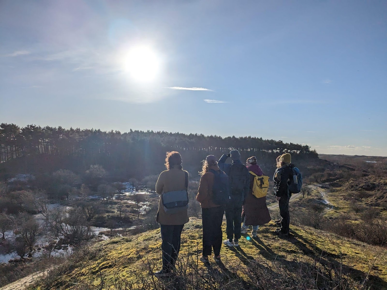 A group of people standing on a hill looking at the sun

Description automatically generated