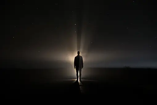A Person is Standing Still in Darkness With a Ray of Light Behind Them