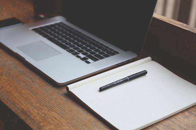 An open laptop with a notebook and pen next to it