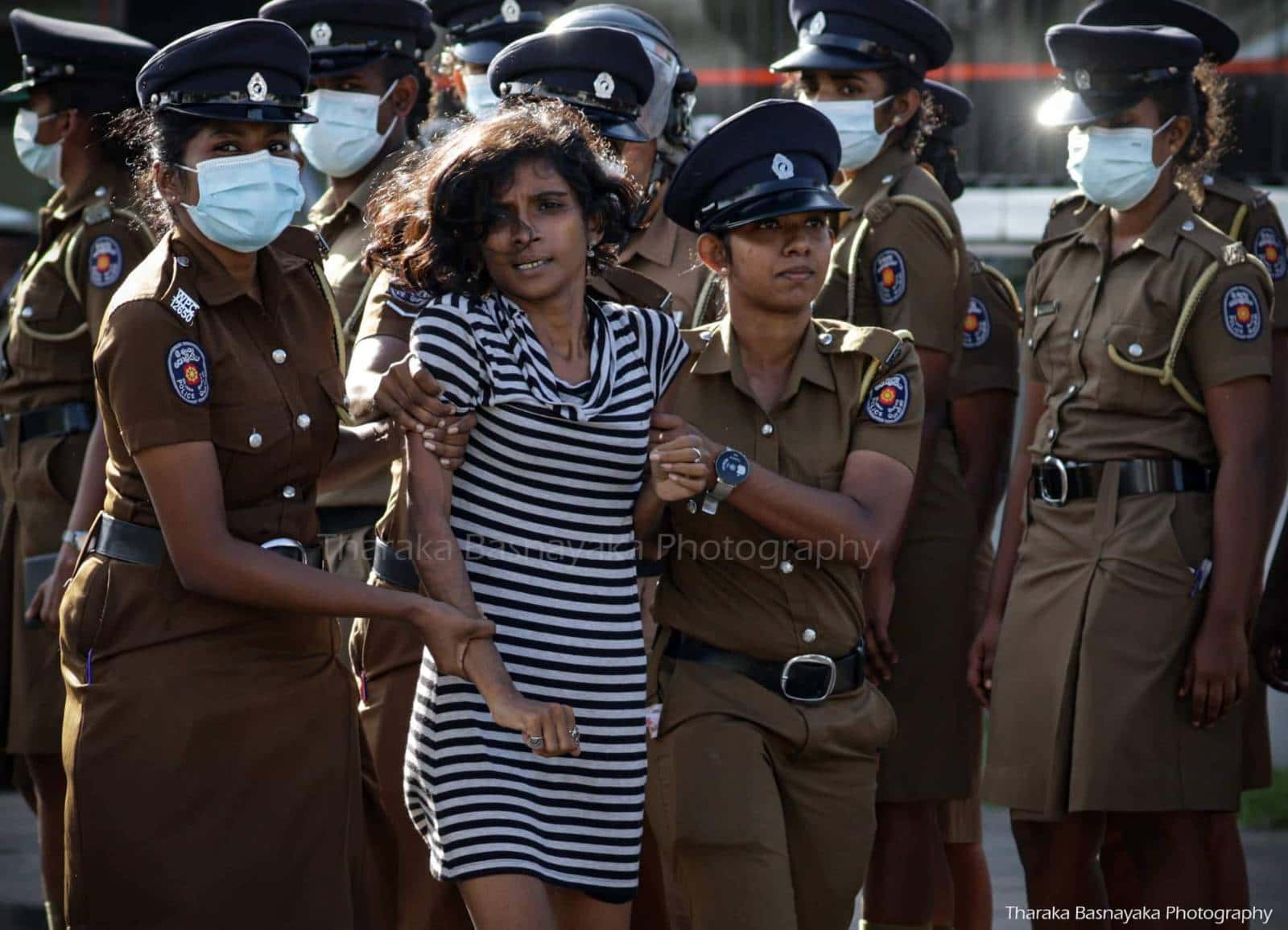 Melani is led away by two female police officers as more police look on.